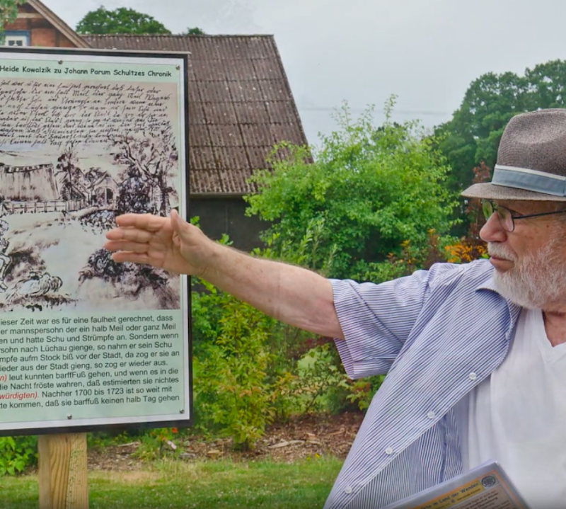 Mann mit Hut zeigt auf ein Informationsschild